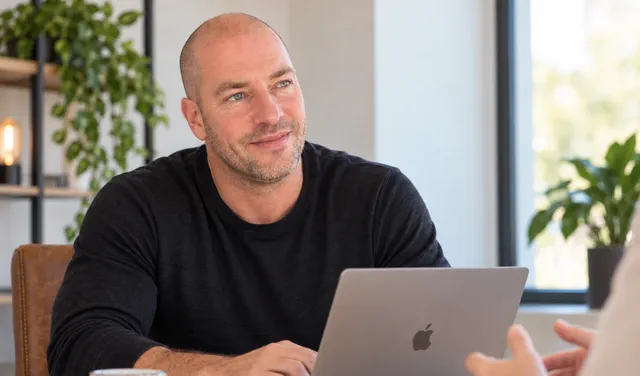 Bas van Beek luistert aan tafel naar een klant, met zijn laptop open.